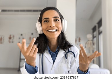 Happy young doctor woman with stethoscope using wireless head phones, speaking from screen, talking on video call at hospital office workplace, smiling, enjoying communication. Head shot portrait - Powered by Shutterstock