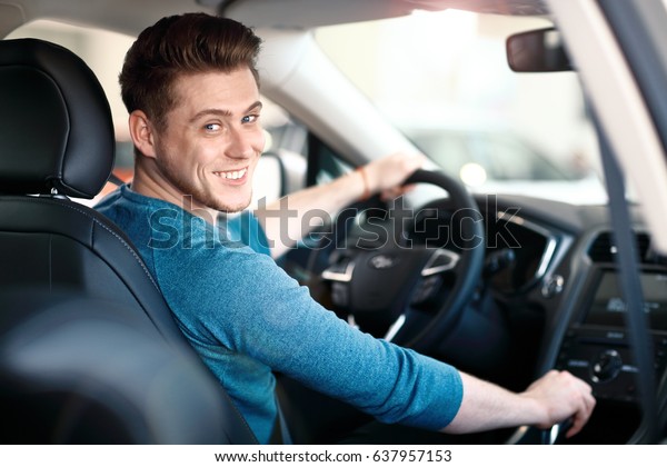 Happy young driver behind the wheel\
inside new car. Lifestyle scene in the car\
dealership