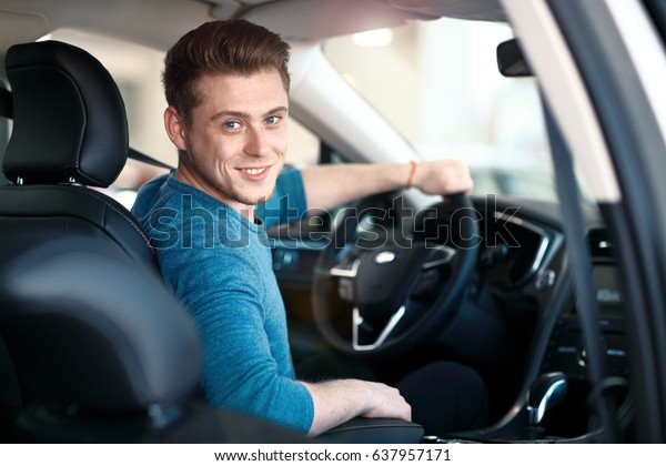 Happy young\
driver behind the wheel inside new\
car.