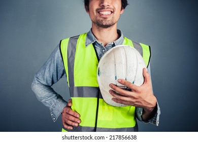A Happy Young Engineer In High Vis Vest Is Holding A Hard Hat