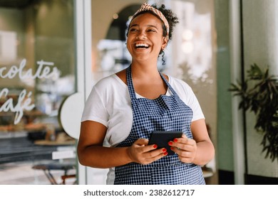 Happy young entrepreneur embraces technology in a vibrant café, holding a digital tablet in hand. Female cafe owner stands confidently in her successful small business. - Powered by Shutterstock