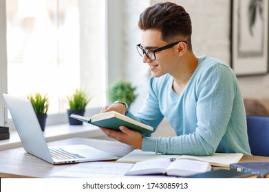 Happy young ethnic man in glasses smiling and reading textbook while sitting at table and doing homework at home
 - Powered by Shutterstock