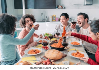 Happy young ethnic woman spoon feeding male friend with delicious pasta in kitchen. Friends eating together - Powered by Shutterstock