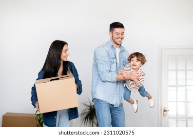 Happy Young European Family Of Three Having Fun On Moving Day, Laughing And Enjoying Relocation, Cheerful Father Lifting Smiling Child In Air While Mother Carrying Cardboard Box With Belongings - Shutterstock ID 2311020575