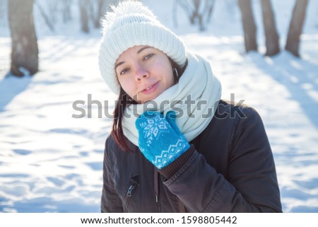 Happy young european woman in white knitted hat and scarf and blue holiday mittens laughing under the snow
