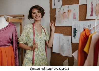 Happy young excited fashion designer poses near mannequin and holds measuring tape. Cheerful lady in floral dress smiles sincerely. - Powered by Shutterstock