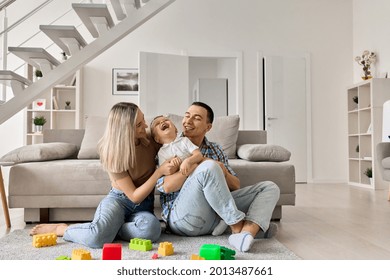 Happy young family with boy child playing enjoying time together at home in living room, parents with child sitting on floor near sofa, mom and dad holding and kissing boy, laughing and having fun. - Shutterstock ID 2013487661