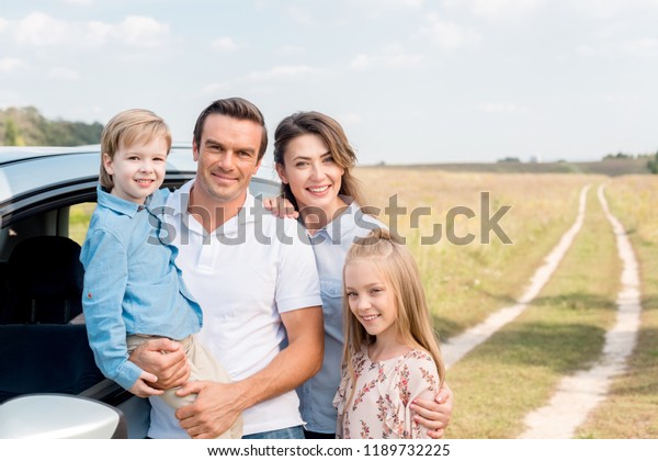 happy\
young family with car looking at camera in\
field