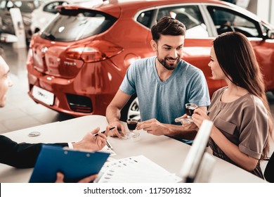 Happy Young Family Are Choosing A New Car In Showroom. Dialogue With Dealer. Cheerful Customer. Automobile Salon. Make A Decision. Cup Of Coffee. End Of A Deal. Good Offer. Buyer And Seller.