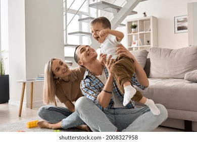 Happy Young Family Couple Having Fun Playing With Cute Small Toddler Kid Son In Modern Living Room Together. Smiling Parents Mum And Dad Enjoying Spending Time With Cute Funny Child Boy At Home.