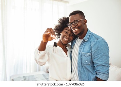 Happy young family couple holding key to new home on moving day concept, first time real estate owners man husband embrace woman wife look at camera proud buying property stand in own flat with boxes - Shutterstock ID 1899086326