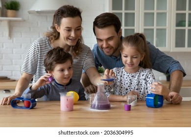 Happy young family couple and sibling kids engaged in learning chemical game, imitating experiment, pouring colorful liquids from beakers to bottles. Parents helping children to study science at play