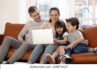 Happy Young Family With Cute Preschooler Kids Have Fun At Home Watching Movie On Laptop Together, Loving Parents And Little Children Relax In Living Room Smile Enjoying Cartoon On Computer