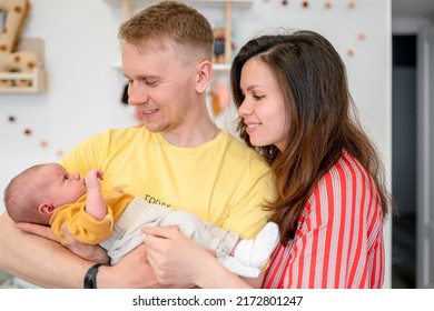 Happy Young Family With Dad, Mom And Newborn Baby In The Baby's Room