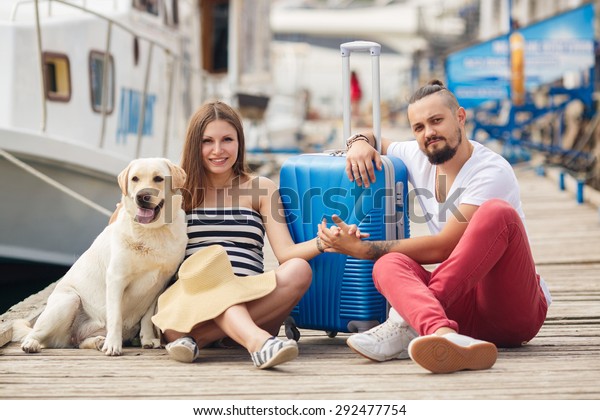 Happy young family with dog and
suitcase. Pregnant woman with husband by the sea. Family on
vacation. Summer holiday and  travel concept. Family portrait
outdoor