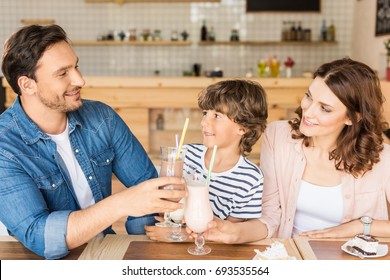 Happy Young Family Drinking Milkshakes In Cafe And Spending Time Together