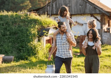 Happy young family enjoy spending time together on weekend at the countryside. Mother, father and two kids walking near their wooden country house. Moving from urban areas to rural areas concept. - Shutterstock ID 2281341545