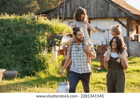 Happy young family enjoy spending time together on weekend at the countryside. Mother, father and two kids walking near their wooden country house. Moving from urban areas to rural areas concept.