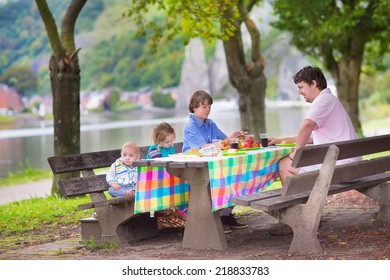 Happy Young Family, Father With Three Children - Boy, Toddler Girl And Little Baby Enjoying  Picnic Sitting On A Bench Having Fruit And Sandwich For Lunch Outdoors During A Trip To Dinant, Belgium