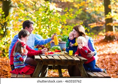 Happy Young Family With Four Children Grilling Meat And Making Sandwich And Salad On A Picnic Table In Sunny Autumn Park. Barbecue Fun For Parents With Kids On Warm Fall Day. Grill And BBQ Party.