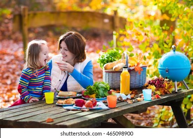 Happy Young Family With Four Children Grilling Meat And Making Sandwich And Salad On A Picnic Table In Sunny Autumn Park. Barbecue Fun For Parents With Kids On Warm Fall Day. Grill And BBQ Party.