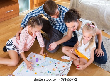 Happy Young Family Of Four Playing At Board Game In Domestic Interior