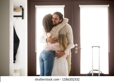 Happy young family in hallway near entrance door at home. Husband hugging wife and little preschool daughter with tenderness and love, with suitcase luggage arrived from business trip, reunion concept - Powered by Shutterstock