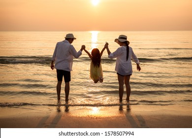 Happy Young Family Have Fun On Beach At Sunset. View From Behind.