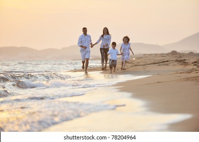 Happy Young Family Have Fun On Beach Run And Jump  At Sunset