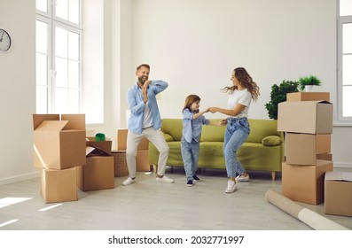 Happy Young Family Having Fun In Their New Home On Moving Day. Cheerful Excited Mum, Dad And Child Playing And Dancing In Room With Sofa And Unpacked Boxes. Real Estate, Mortgage, Buying House Concept