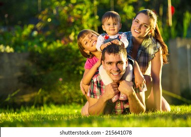 Happy young family having fun outdoors in summer. Mother, father and their cute little daughters are playing in the sunny garden. Happy parenthood and childhood concept. Focus on the father.