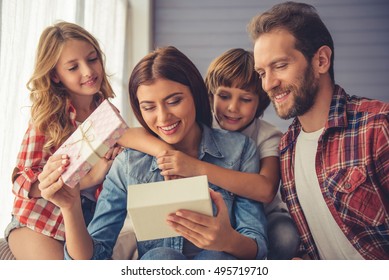 Happy Young Family At Home. Loving Kids And Husband Are Giving A Present To Their Beautiful Mom