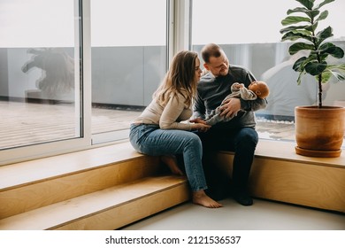 Happy Young Family At Home. Mother And Father Holding Newborn Baby In Arms, Smiling, Looking At Him.