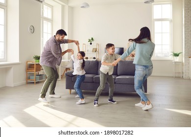 Happy Young Family With Kids Enjoying Free Time On Weekend At Home. Parents And Children Dancing And Having Fun In Spacious Living-room, Celebrating Moving Into New House Or Rented Apartment