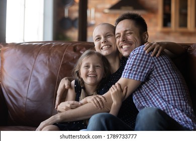 Happy Young Family With Little Daughter With Sick Cancer Patient Bald Mom Hug Cuddle On Couch At Home, Smiling Parents With Ill Hairless Mother Relax With Small Girl Child, Show Love Care Support