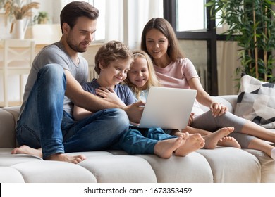 Happy Young Family With Little Kids Sit On Comfortable Couch Relaxing Watching Movie Or Cartoon On Laptop Together, Overjoyed Parents And Small Children Enjoy Funny Video On Computer At Home