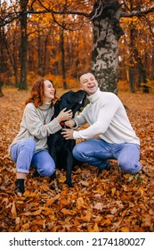 Happy Young Family Man And Woman Have Fun Walking With Their Dog In The Autumn Park, They Adore Their Pet.