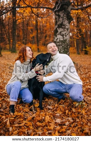 Happy young family man and woman have fun walking with their dog in the autumn park, they adore their pet.