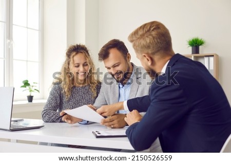 Happy young family at meeting in office signs document on purchase of real estate or loan agreement. Head of bank, realtor or financial advisor submits contract and indicates place of its signing..