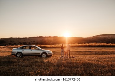 Happy Young Family Mom And Dad With Their Little Son Enjoying Summer Weekend Picnic On The Car Outside The City In The Field At Sunny Day Sunset, Vacation And Road Trip Concept