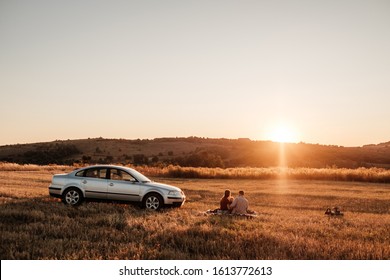 Happy Young Family Mom And Dad With Their Little Son Enjoying Summer Weekend Picnic On The Car Outside The City In The Field At Sunny Day Sunset, Vacation And Road Trip Concept