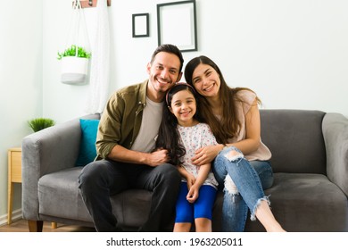 Happy young family of mom, dad and daughter laughing and making eye contact while relaxing together on the living room sofa  - Shutterstock ID 1963205011