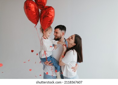 Happy young family mom dad and little daughter have fun with balloons and confetti on Valentine's Day