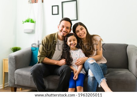 Happy young family of mom, dad and daughter laughing and making eye contact while relaxing together on the living room sofa 