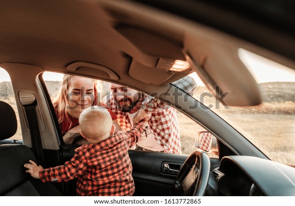 Happy\
Young Family Mom and Dad with Their Son Little Driver Enjoying\
Summer Weekend Picnic on the Car Outside the City in the Field at\
Sunny Day Sunset, Vacation and Road Trip\
Concept