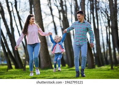 Happy Young Family Of Mother, Father And Little Daughter Having A Great Quality Time In The Park In The Spring