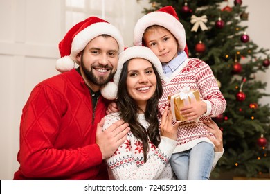 Happy Young Family With One Child Holding Christmas Gift And Smiling At Camera