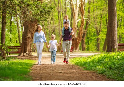 Happy young family parents with a child in a green summer city park have fun walking together