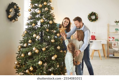 Happy young family parents and children gathering together on Christmas, beautifying their house. Joyful father, mother and two kids preparing to place golden star on top of decorated Christmas tree. - Powered by Shutterstock