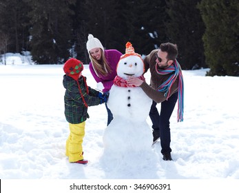 happy young  family playing in fresh snow and making snowman at beautiful sunny winter day outdoor in nature with forest in background Arkivfotografi